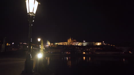 una vista del famoso castillo de praga sobre el río vltava desde el puente de carlos por la noche, durante un cierre de covid-19 sin gente en ninguna parte, linternas y estatuas en el puente, alejar la toma de 4k