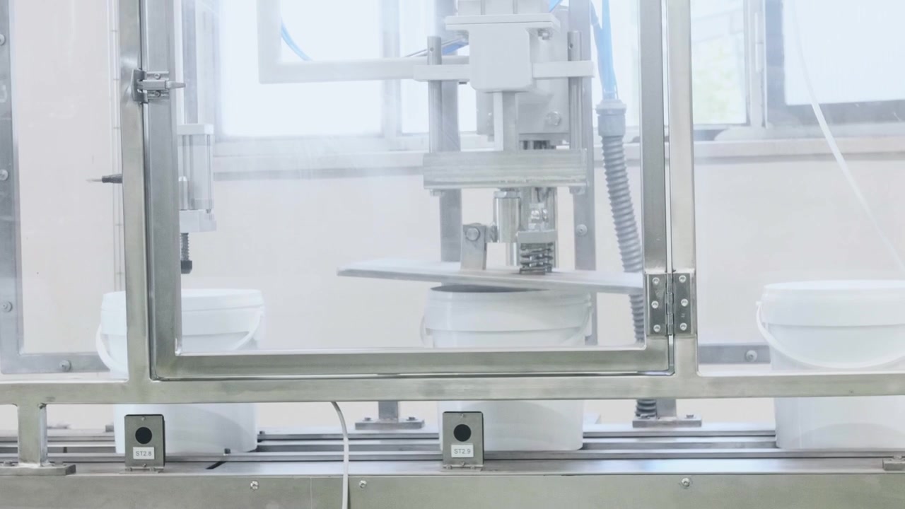 An automated industrial machine sealing white plastic containers on a conveyor belt inside a clean food manufacturing facility, highlighting precision and efficiency in modern production
