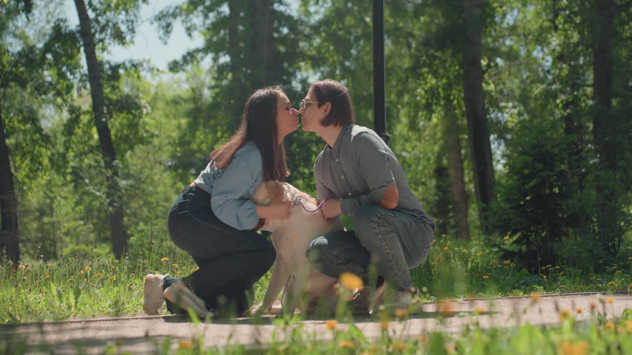 Pareja blanca con un golden retriever sonriendo en la hierba, caricias suaves e indicaciones de adiestramiento, prado al aire libre con dientes de león, gestos de apoyo, correa presente, luz natural, comportamiento canino tranquilo y cooperativo