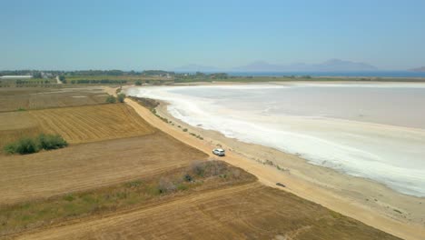 Aerial-View-of-a-White-Vehicle-Driving-Near-The-Salt-Flats-In-Summer-in-Kos,-Greece