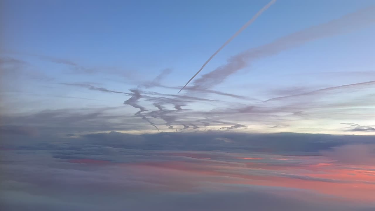 An aerial view taken from a jet cockpit at dawn flying under multiple contrails fading in a pastel color sky, and golden clouds bellow