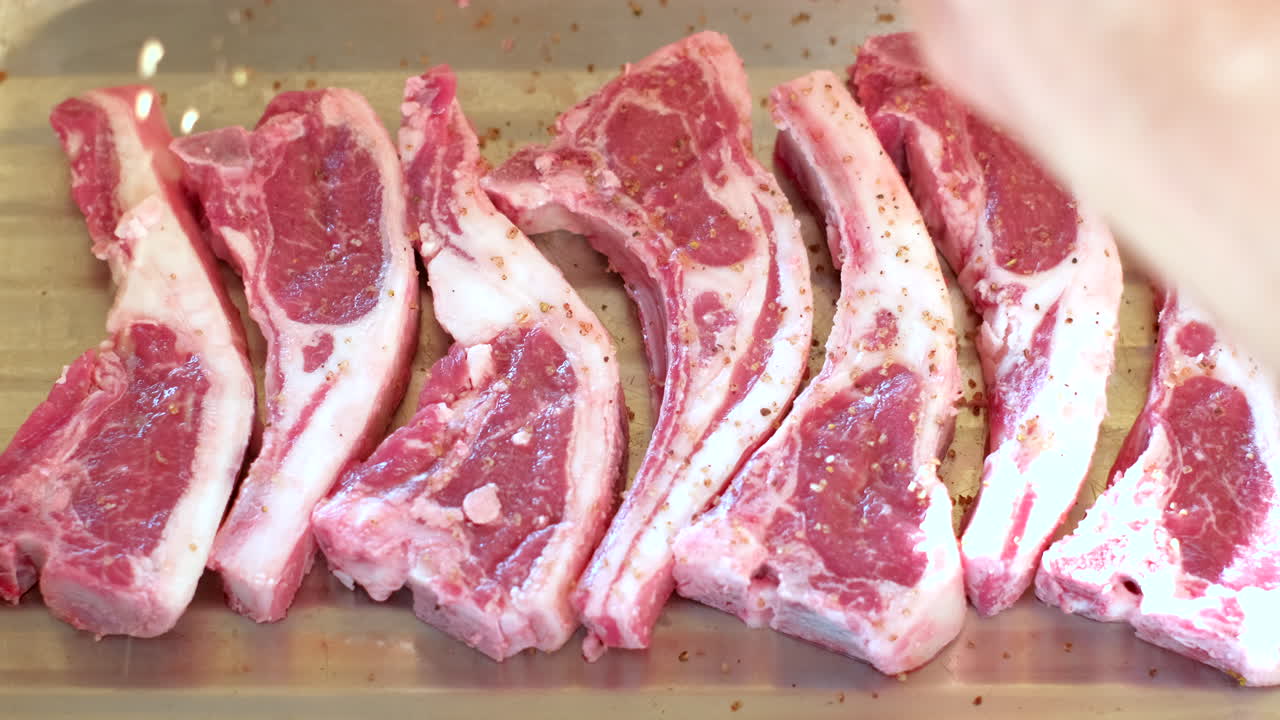 Lamb chops on wooden board being spiced and seasoned before barbecue
