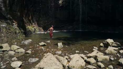 Man-dives-into-waterfall-pool-before-camera-pans-up-to-lush-rock-wall-in-forest