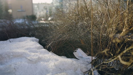 slow pan of white face mask on snowy ground by bush, car passes