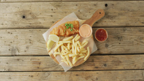 Vídeo-De-Pescado-Y-Patatas-Fritas-Sobre-Tabla-De-Madera-Con-Salsas,-Con-Espacio-Para-Copiar-Sobre-Mesa-De-Madera