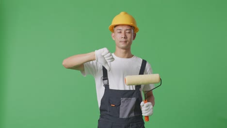 asian man painter wearing safety helmet showing thumbs down gesture to camera while standing in the green screen background studio