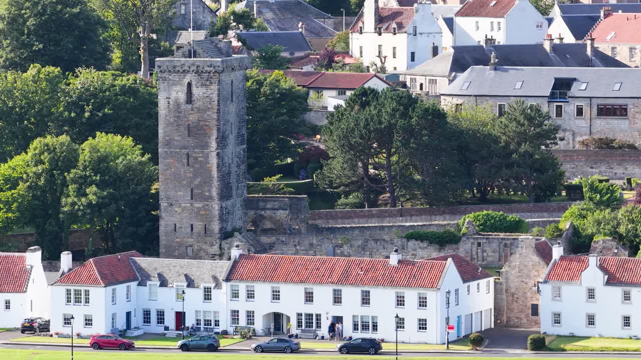 Daytime pan reveals medieval stone tower, village houses, lush greenery, and bright natural lighting