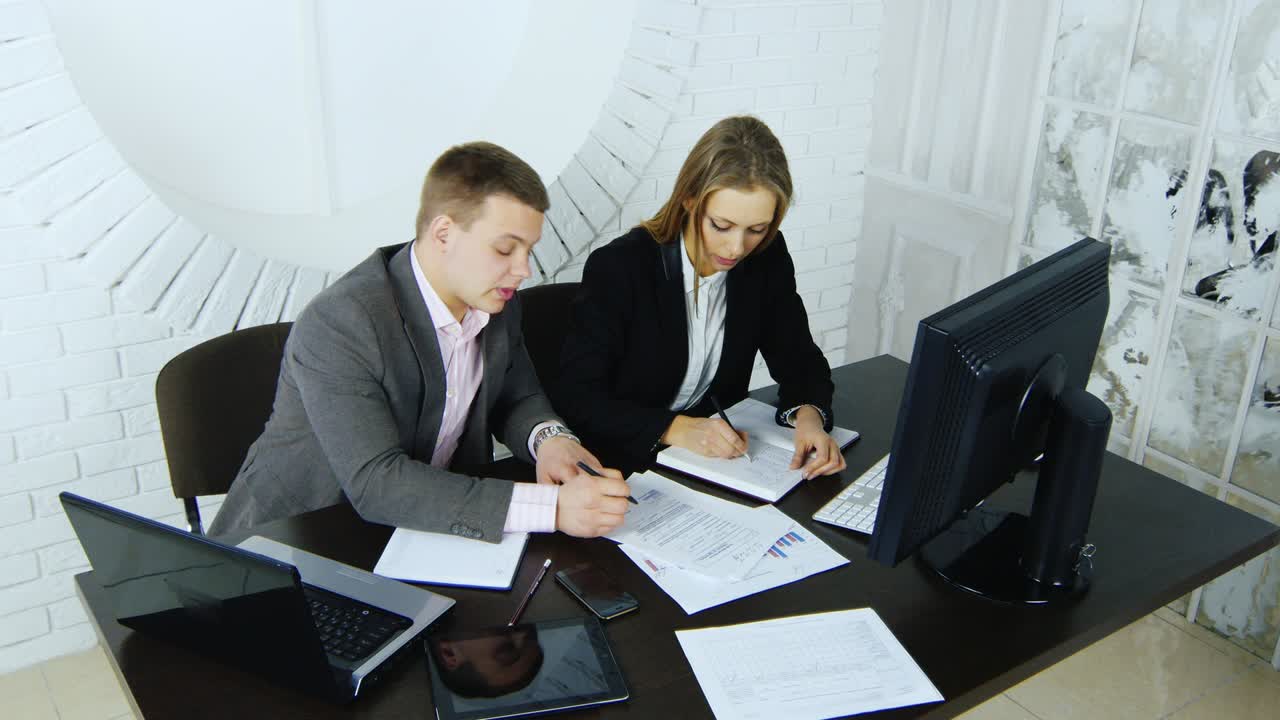 el director discute con su secretario los proyectos en la mesa con una computadora y una computadora portátil