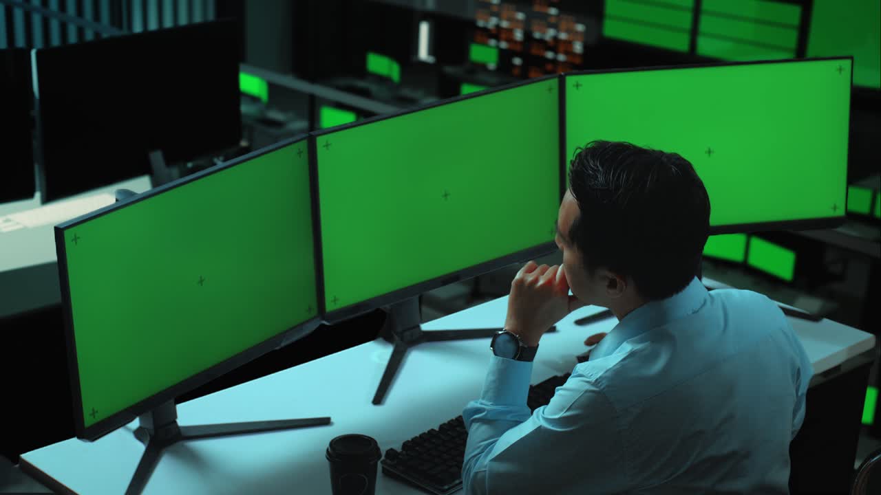 vista lateral de un hombre asiático pensando en algo mientras trabaja con múltiples monitores de computadora simulados en la oficina