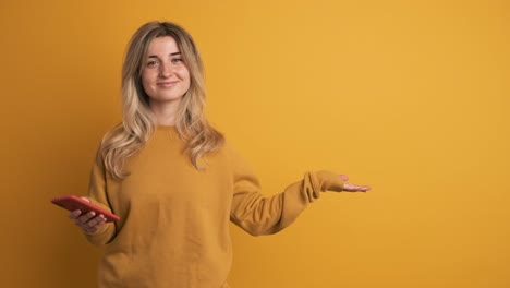 cheerful young woman with smartphone showing empty wall space on yellow background