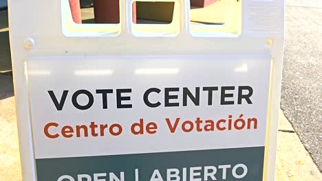 a bilingual sign “vote center, centro de votación – open, abierto” with spanish translation is shown outdoors, representing inclusivity, registration services, mail ballot support and in-person voting