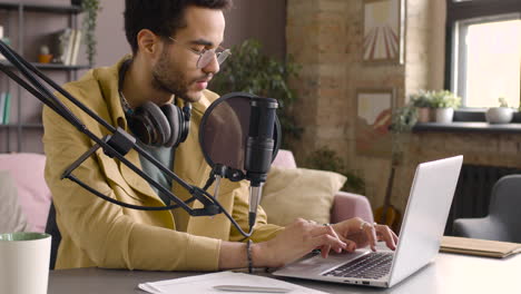 Mann-Mit-Brille-Sitzt-An-Einem-Tisch-Mit-Mikrofon-Und-Schreibt-Auf-Laptop-1