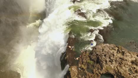 Una-Vista-Aérea-Muestra-A-Los-Turistas-Nadando-En-La-Cima-De-Las-Cataratas-Victoria-En-La-Piscina-Del-Diablo-En-Zambia