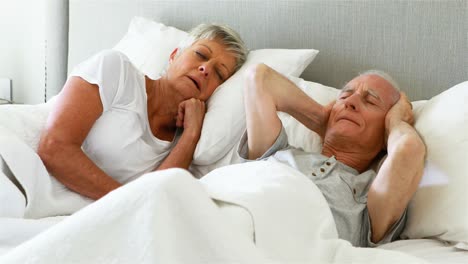 senior man covering his ears while woman snoring in bedroom