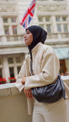 vertical video portrait of smiling muslim businesswoman wearing hijab and modern business suit standing outside city office buildings 6