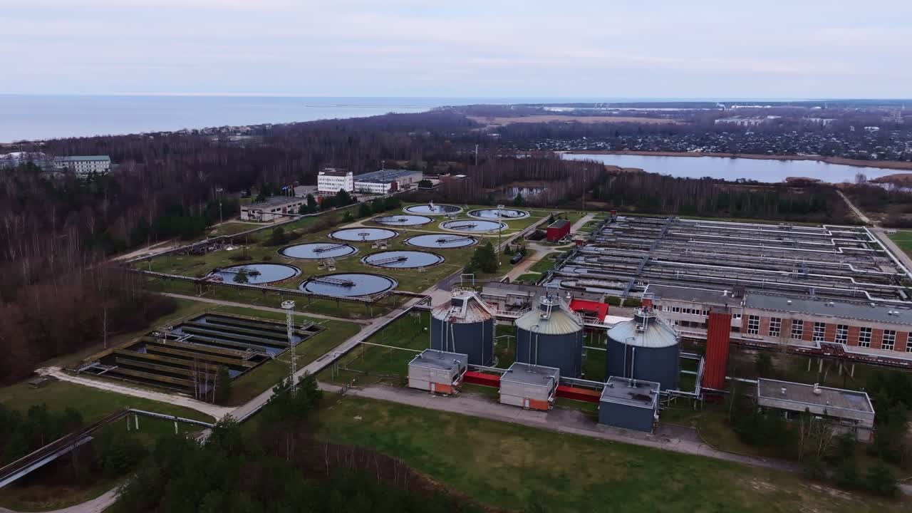Drone films circular basins and tanks at wastewater plant near Baltic coastline