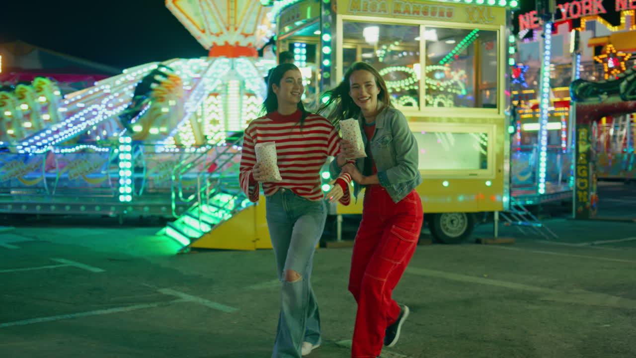 가장 친한 친구들이 함께 조명된 루나 파크에서 즐거움을 나누고 있습니다. 행복한 소녀들이 고 있습니다.