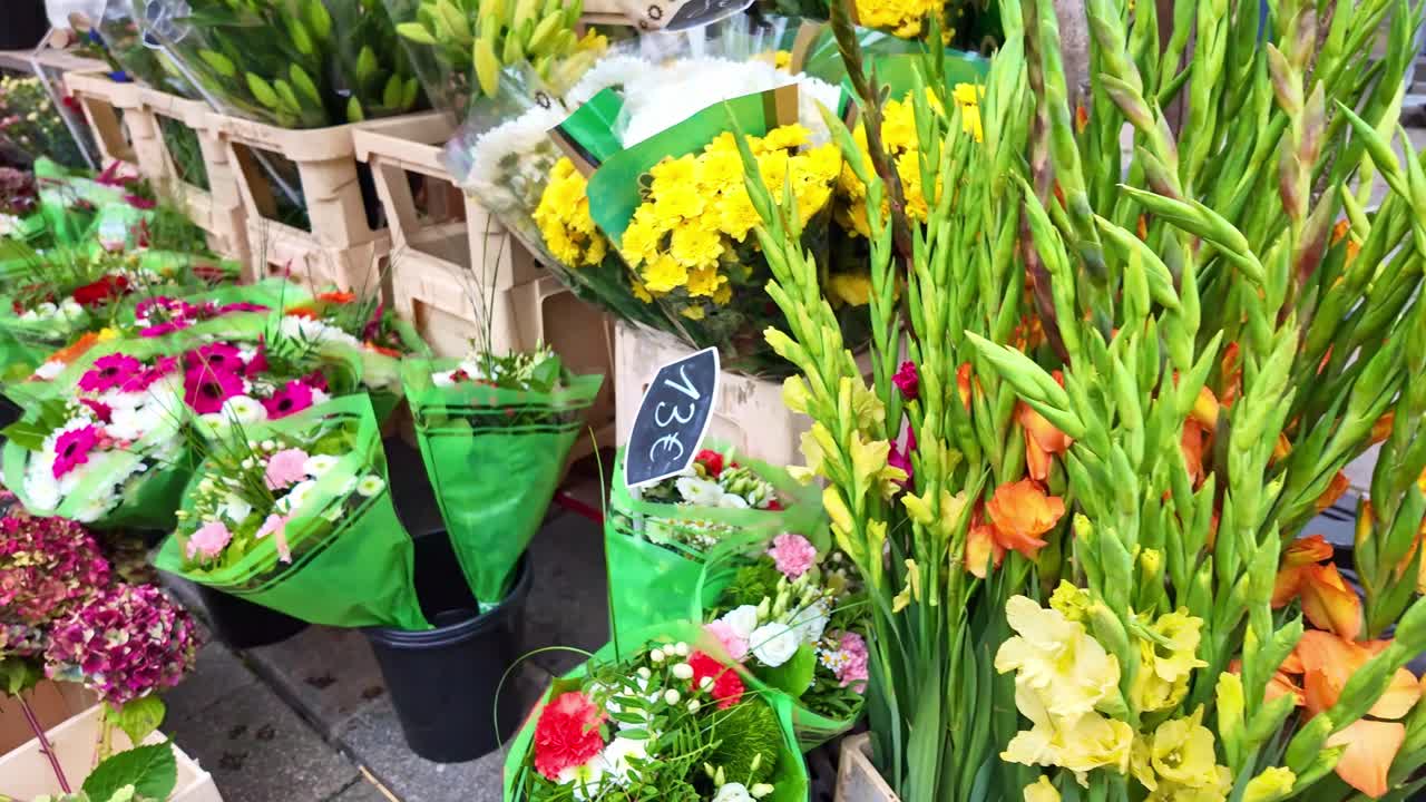Market flower shop display with bouquets and potted plants arranged in wooden crates on a sidewalk