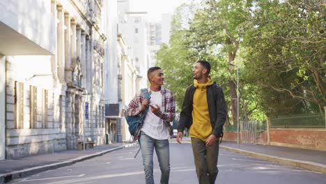 two happy mixed race male friends walking and talking with backpacks