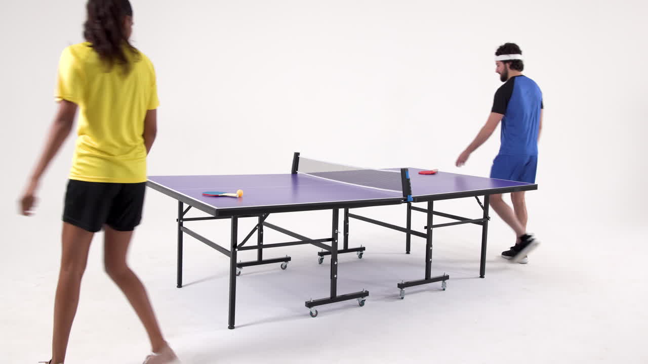 Playing table tennis, man and woman competing in studio setting