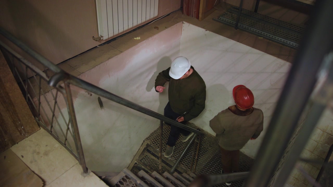 Pianerottolo interno tranquillo visto dall'alto, con ringhiere e gradini metallici in primo piano, un pavimento chiaro e luminoso e un termosifone vicino alla parete di fondo.