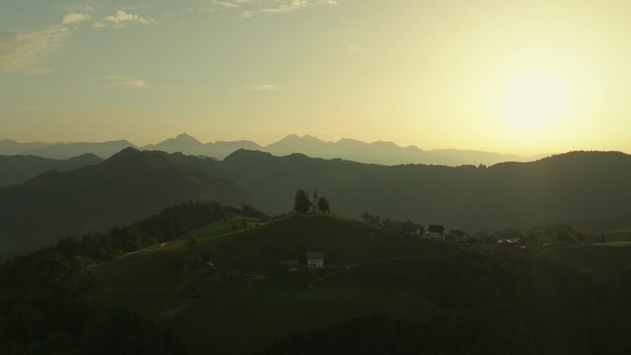 Golden sunrise over St. Thomas Church with rolling hills and distant Slovenian Alps in the background