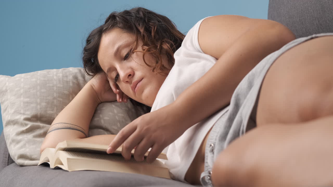 Donna che legge un libro sdraiata sul divano del soggiorno.