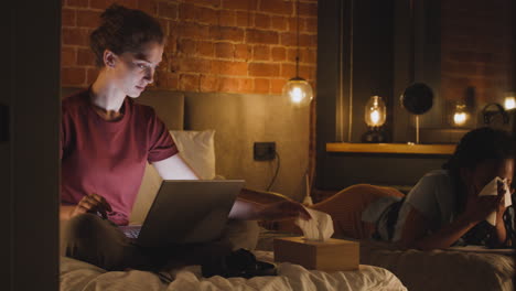 chica viendo videos en una laptop mientras se limpia la cara con una toalla de papel en el dormitorio por la noche