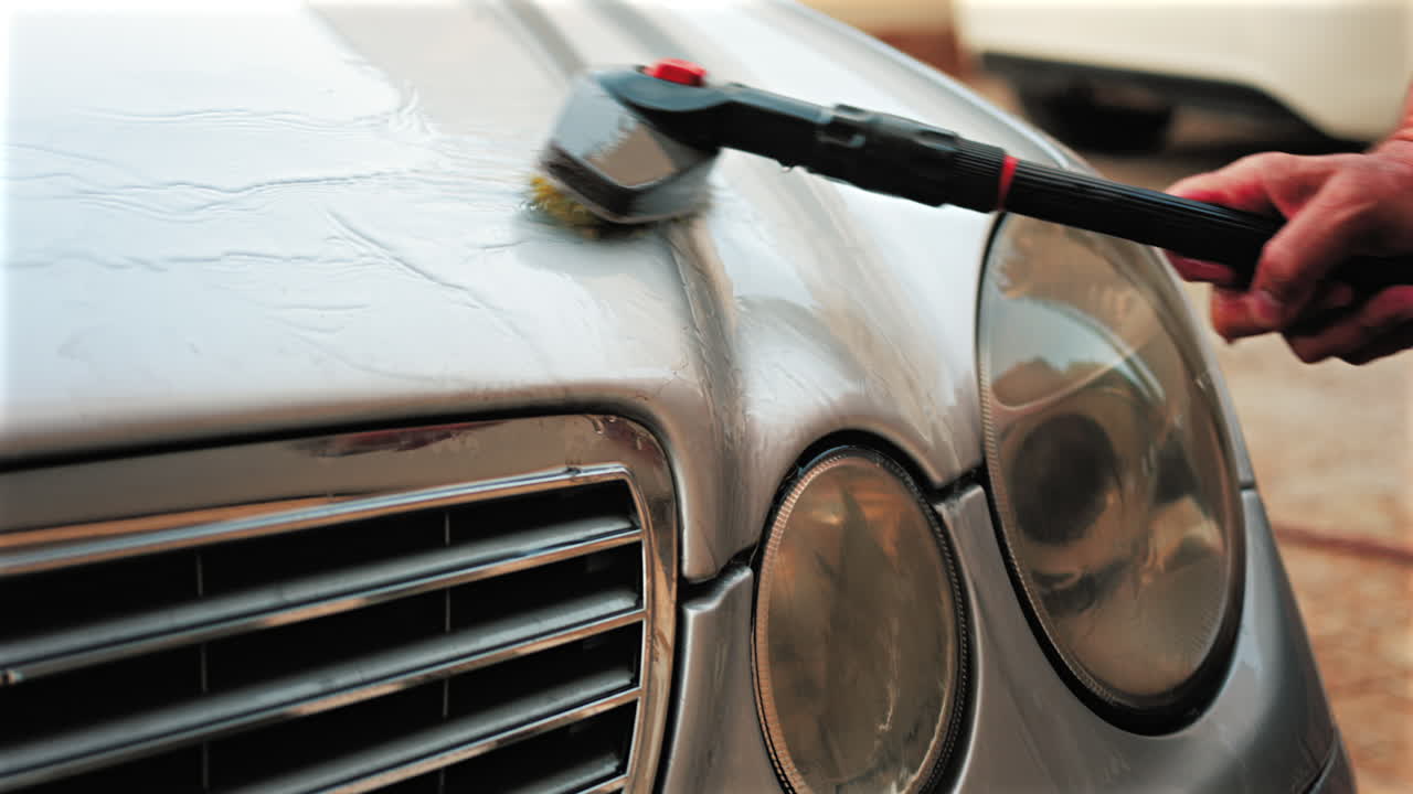 Close up of a car hood being scrubbed with a brush and water