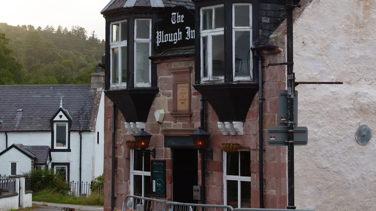 Camera pans down The Plough Inn facade, soft evening light, tranquil Highland village setting