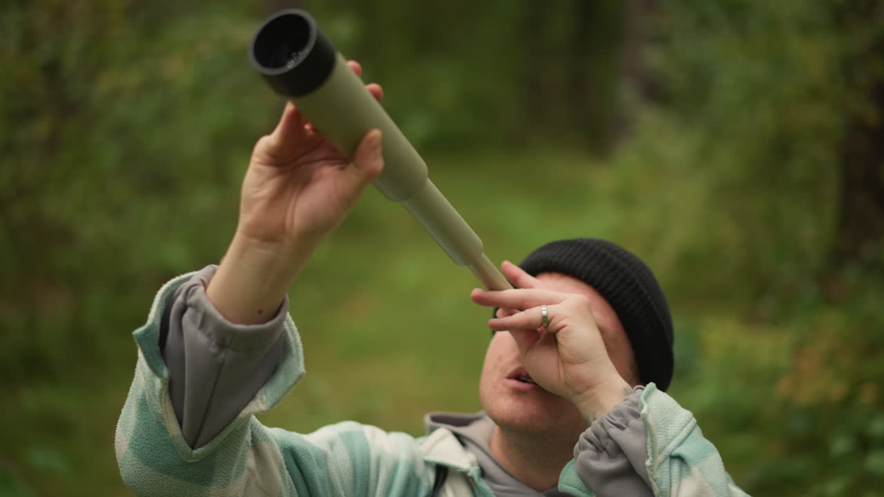 Uomo bianco in una foresta muschiosa che scruta con un cannocchiale, regolando la messa a fuoco mentre osserva la volta alla ricerca di uccelli e punti di riferimento, atmosfera calma e contemplativa, berretto di lana nero, sfondo bokeh verde, zaino visibile