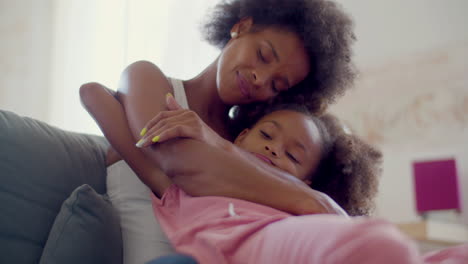 loving black woman and cute little girl sitting on couch and hugging at home