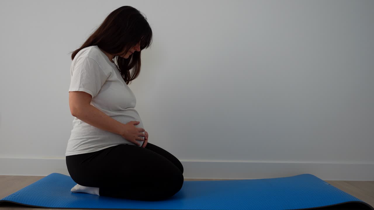 Pregnant touching her belly on a blue mat before starting to exercise