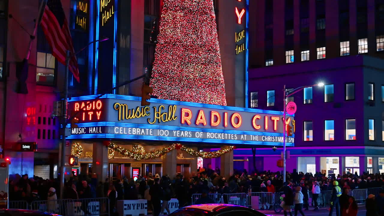 New York, USA, 12. december 2025: Indgangen til Radio City Music Hall dekoreret med en kæmpe juletræsguirlande. Menneskemængder går forbi på gaden i New York, USA om natten.