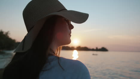 chica con sombrero para el sol mirando el agua durante la puesta de sol