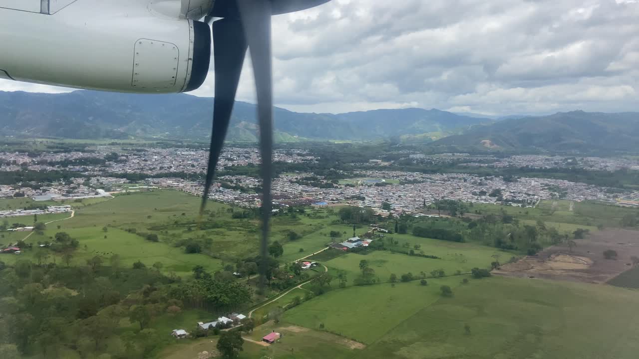 vista por la ventana de las hélices de un pequeño avión que aterriza en una ciudad tropical verde