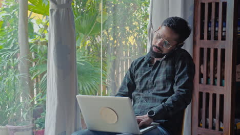 man working at home using laptop got frustrated while talking on phone