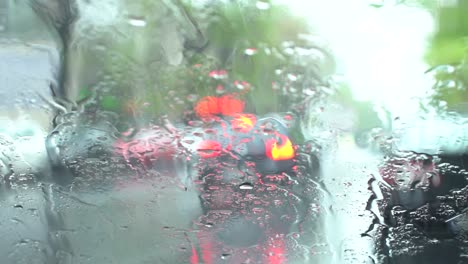 Regentropfen-In-Zeitlupe,-Die-Auf-Ein-Autofenster-Fallen,-Mit-Bokeh-Ampeleffekten-Im-Hintergrund