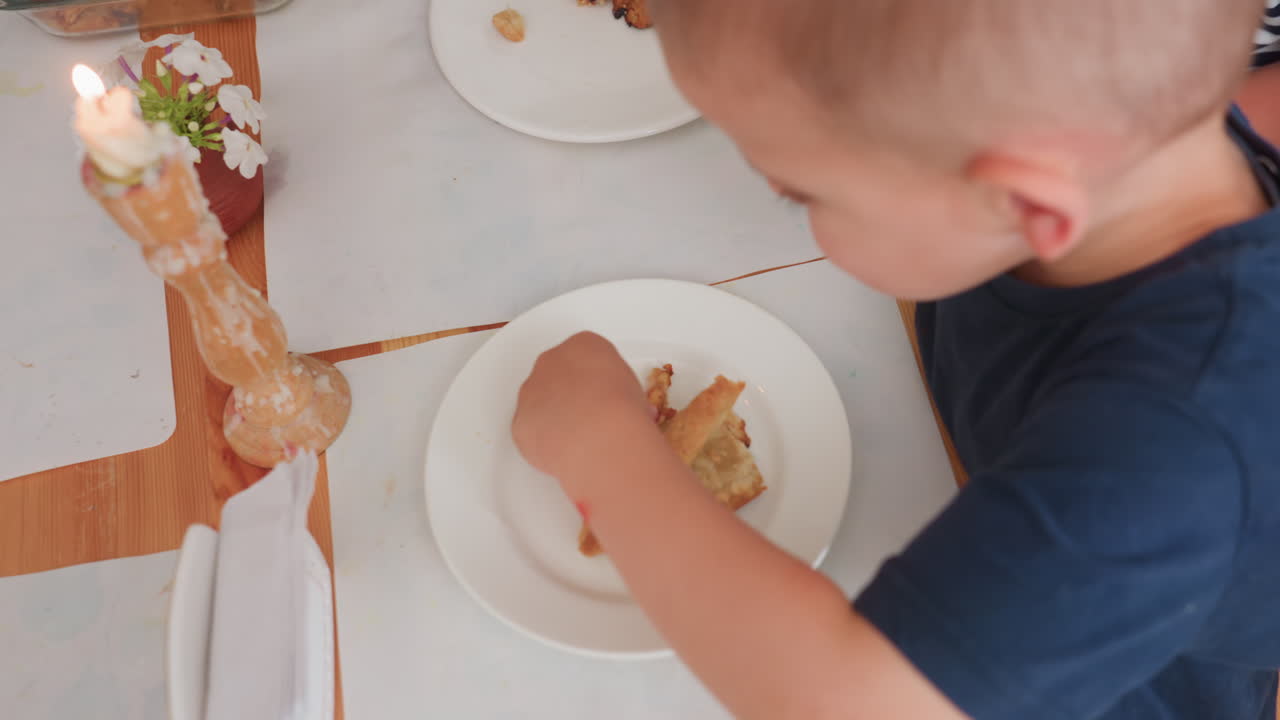 Vista della mano di un adulto che serve cibo ai bambini mentre uno di loro guarda: una mano sinistra raccoglie una calda torta di mele da un piatto di vetro con un coltello e un cucchiaio e la mette su piatti bianchi durante una merenda in classe.
