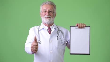 handsome senior bearded man doctor against green background