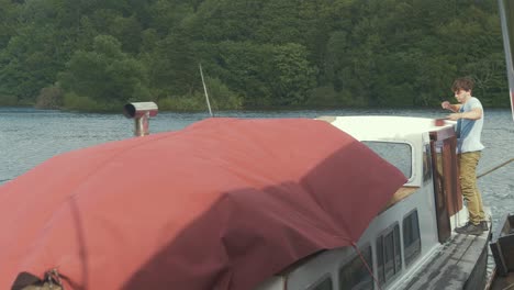 young man aboard wooden boat wipes dust off wooden liveboard boat