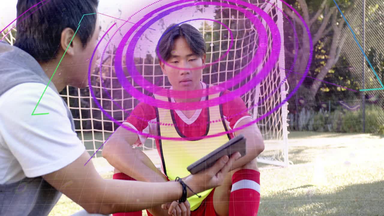 Coach kneeling by player presenting tablet, rings overlaying faces and net during soccer coaching