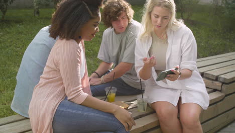 joven rubia mostrando algo interesante en el teléfono móvil a sus amigos multiétnicos en un parque