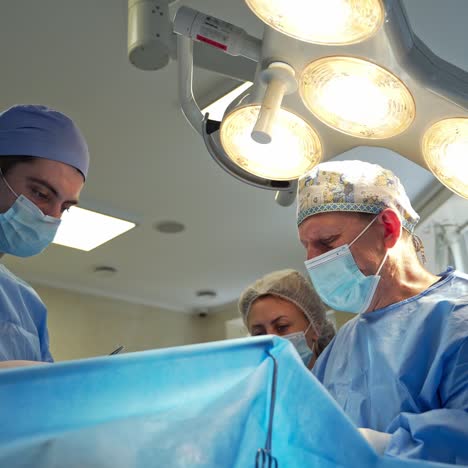 medical specialists concentrated on operation. male surgeons and female assistant performing surgery in operating room. view from below