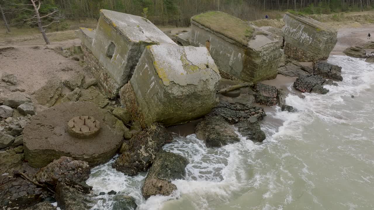 카로스타 북부 요새, 발트해 연안, 큰 파도, 흐린 날, 느린 동작, 뒤로 움직이는 드론 샷에 있는 버려진 해변 요새 건물의 아름다운 공중 전망
