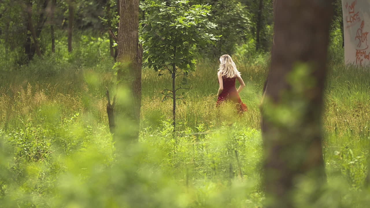 Blond Woman in Red Dress runs through the bright green woods. She is lost and looking for her grandmothers home. Beautiful slow motion.