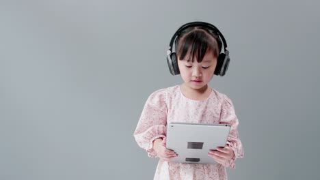 girl with earphone dancing holding digital tablet in studio with gray background