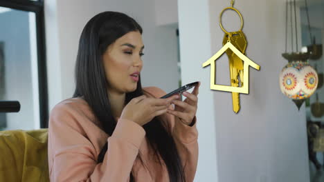 animación de llave de casa de oro y llave fob sobre mujer biracial feliz usando teléfono inteligente en casa