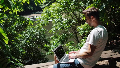 man working on laptop outdoors in lush green nature