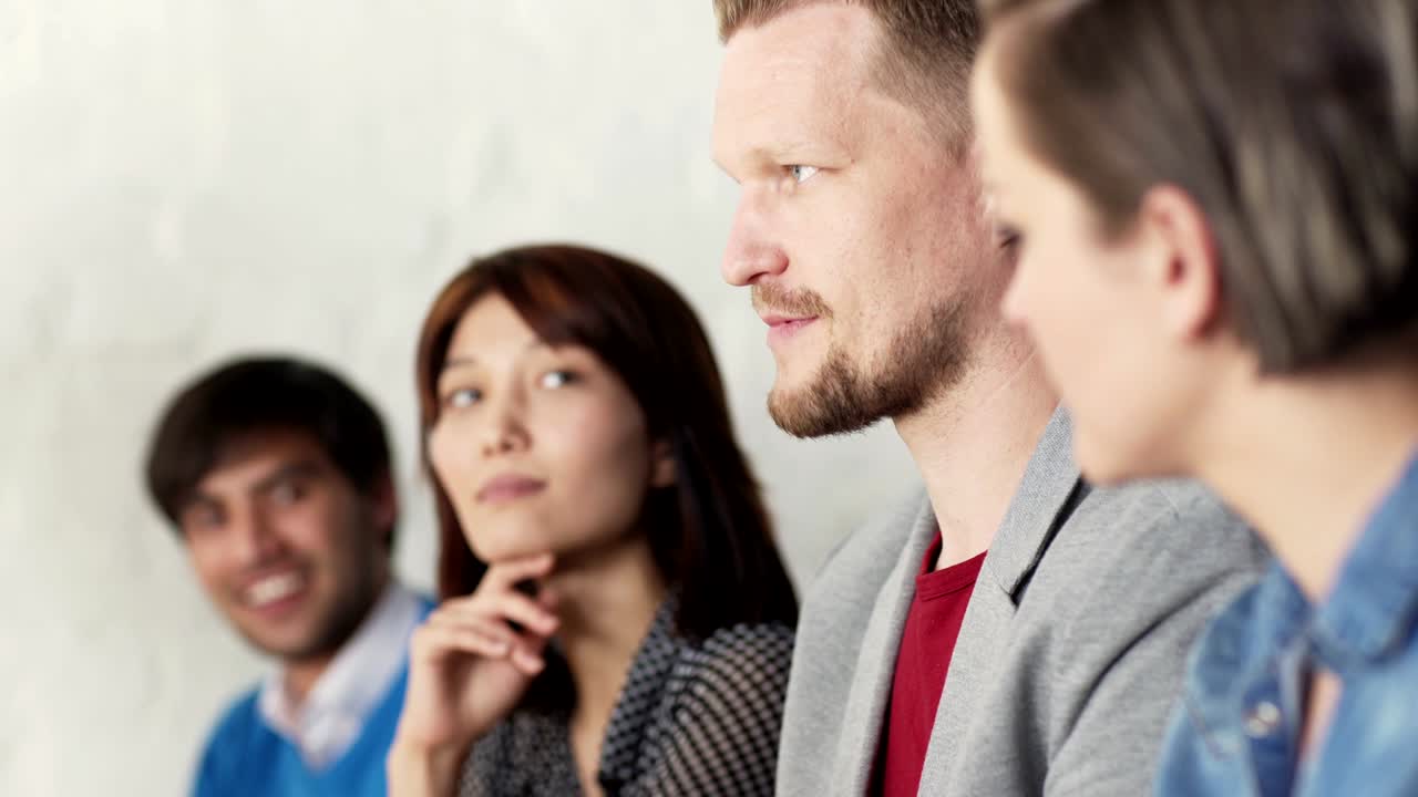 Tracking shot closeup of multi-ethnic business people sitting at conference during presentation and listening to colleague telling stories. Selective focus on middle aged man talking